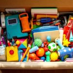 Une boîte de rangement ouverte contenant divers objets colorés tels que des livres, des jouets et des outils, disposée dans une pièce bien éclairée, créant une ambiance chaleureuse et accueillante.