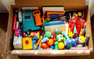 Une boîte de rangement ouverte contenant divers objets colorés tels que des livres, des jouets et des outils, disposée dans une pièce bien éclairée, créant une ambiance chaleureuse et accueillante.