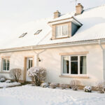 Maison familiale en hiver avec jardin légèrement enneigé, toiture et gouttières visibles, éclairée par une douce lumière matinale.