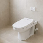 Toilettes contemporaines lumineuses avec un abattant lavant électrique blanc installé sur une cuvette standard, une arrivée d’eau et une prise murale discrètes.